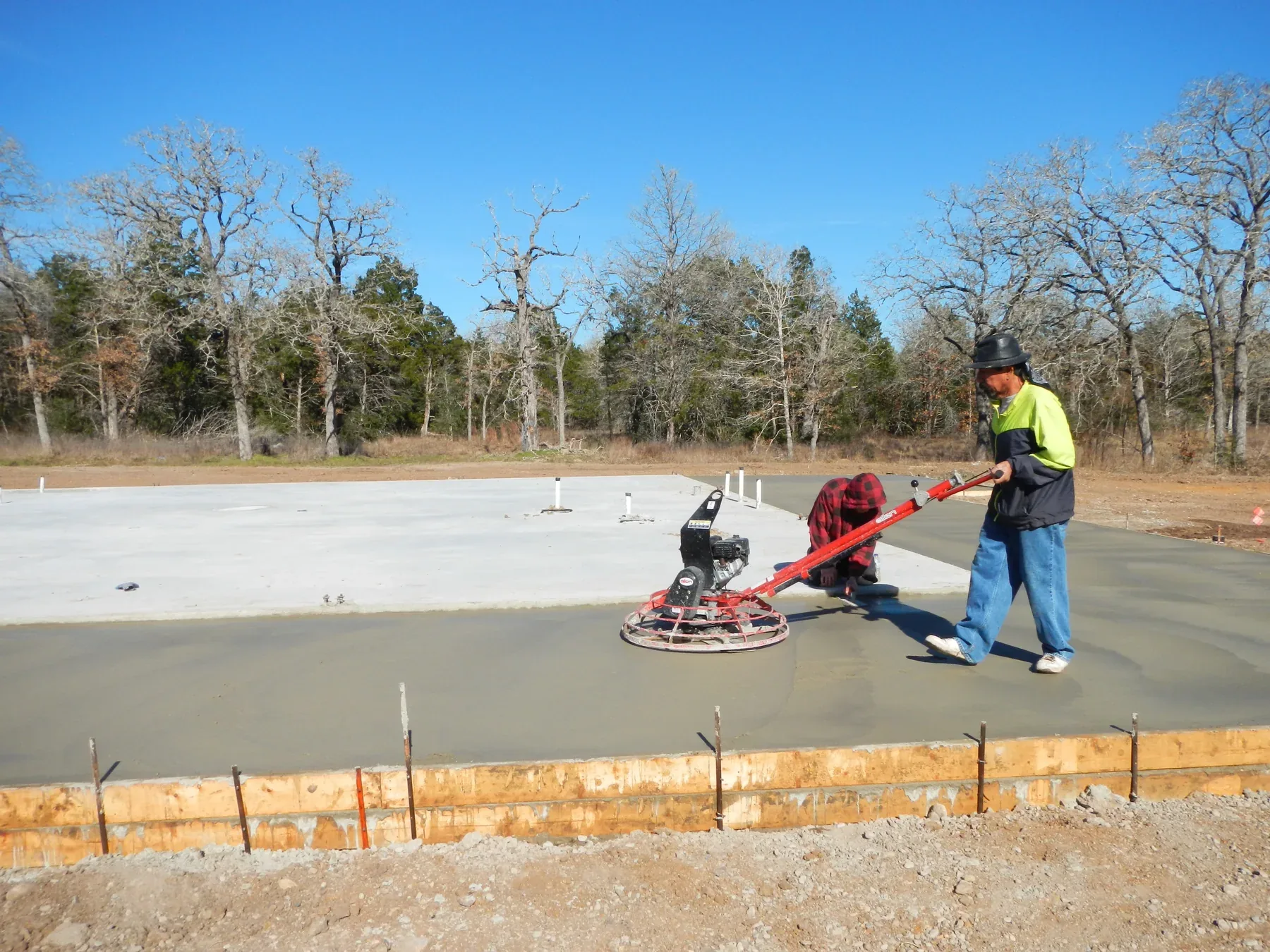 Concrete finisher running a power trowel across a freshly poured building slab