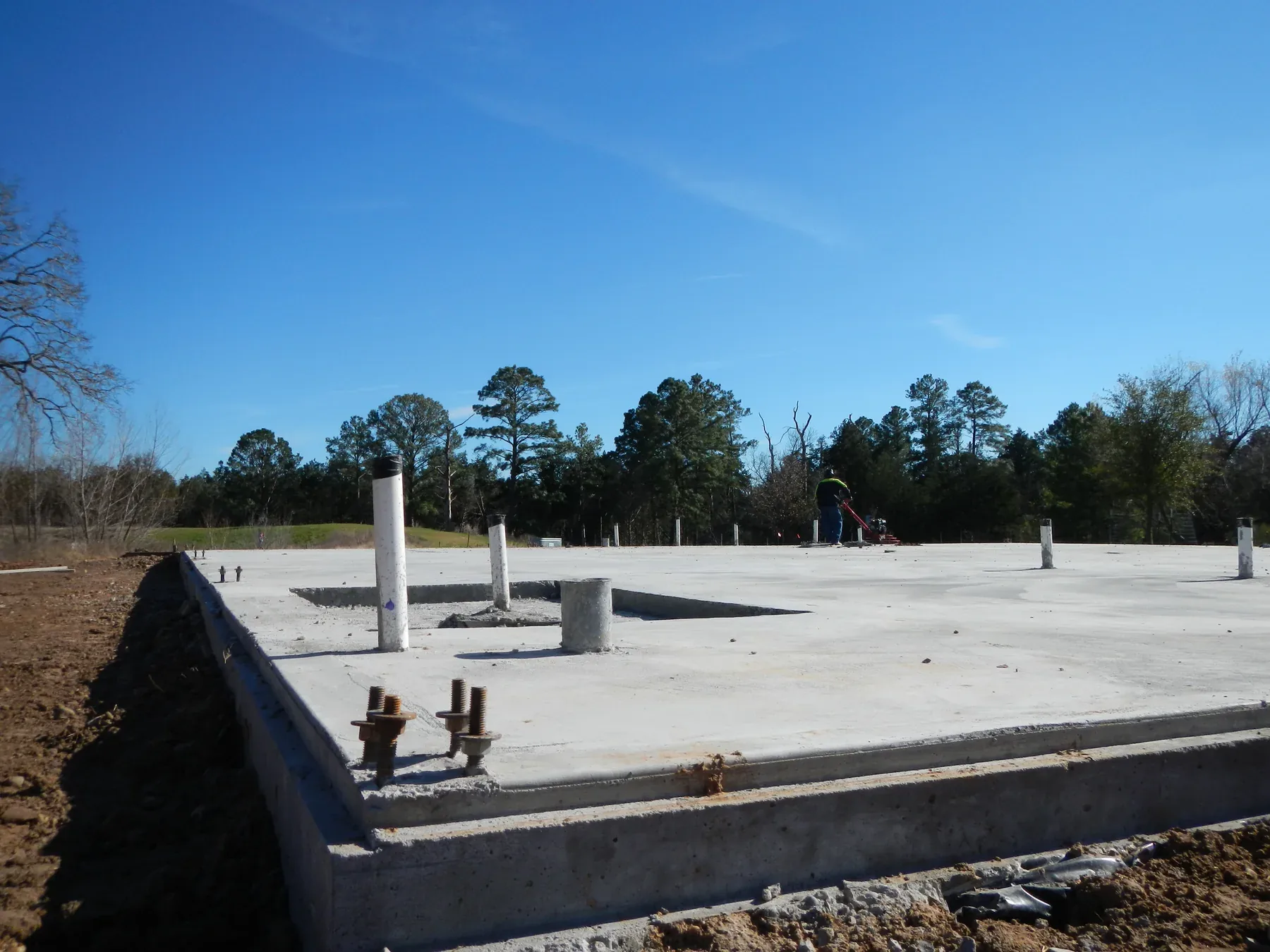 Finished concrete slab with anchor bolt piers along the perimeter, ready for frame erection