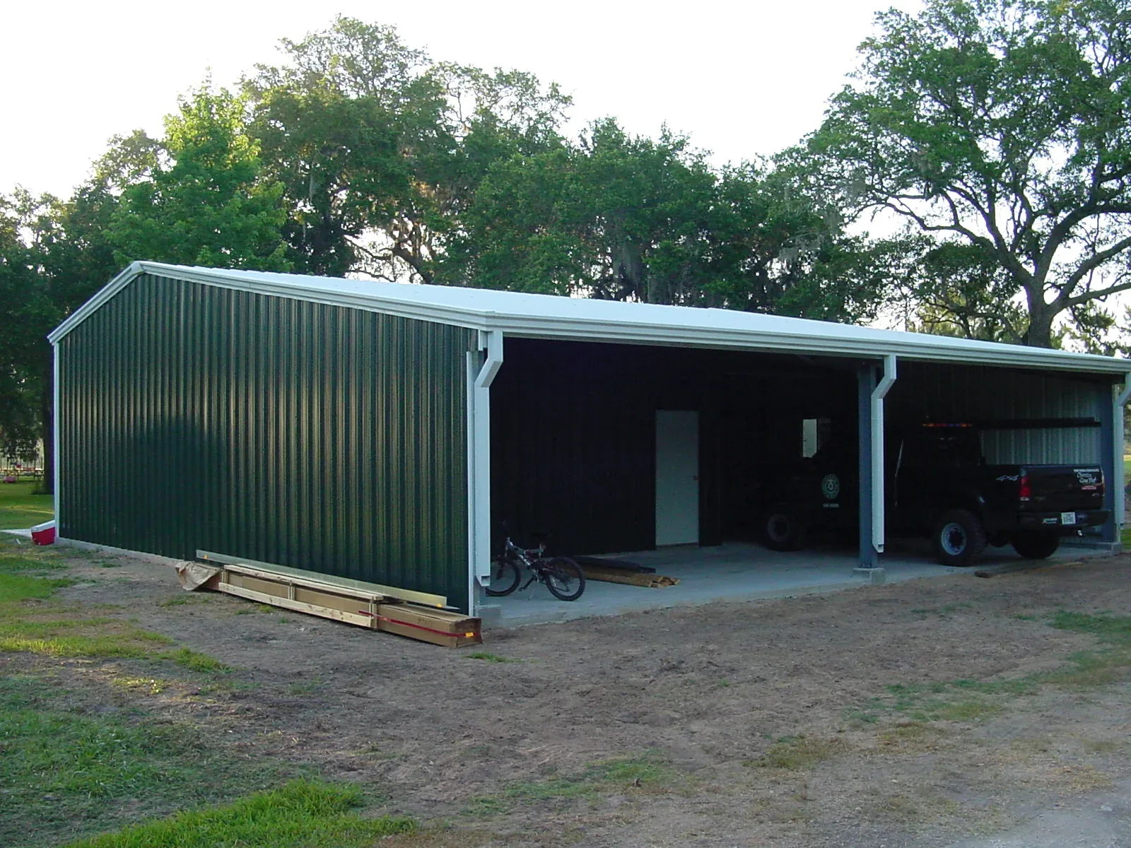 Green metal shop building with an open lean-to bay running along one side