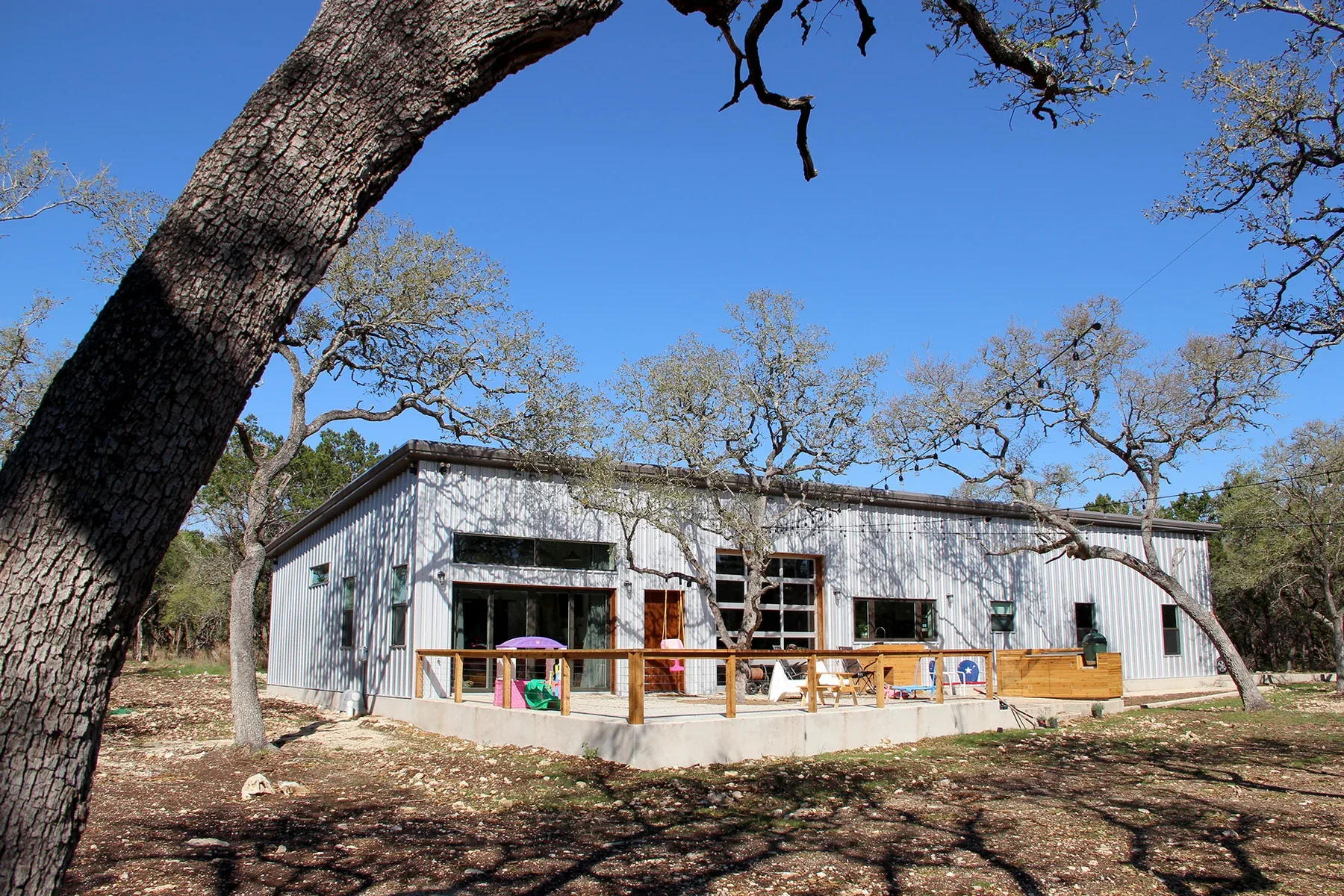Metal barndominium with a standing-seam roof set among mature live oaks in the Texas Hill Country