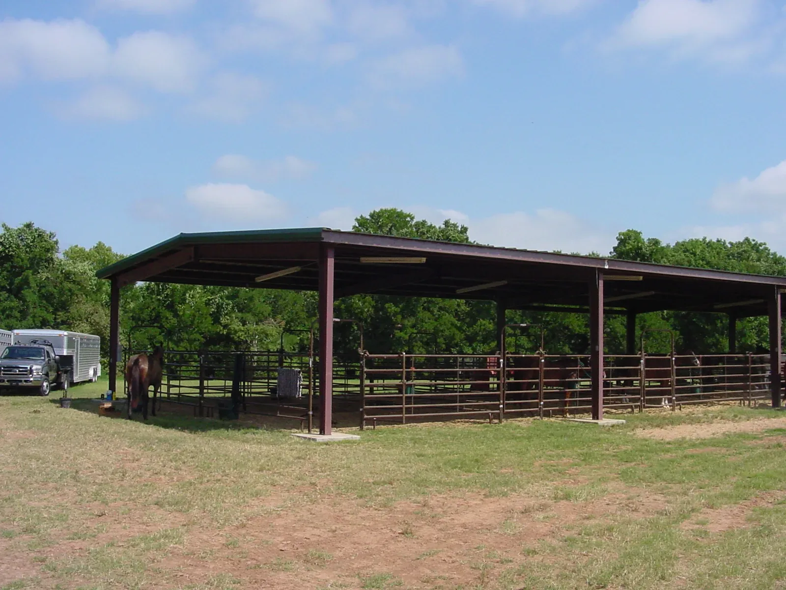 Open-sided steel livestock shelter over a fenced pen on open pasture