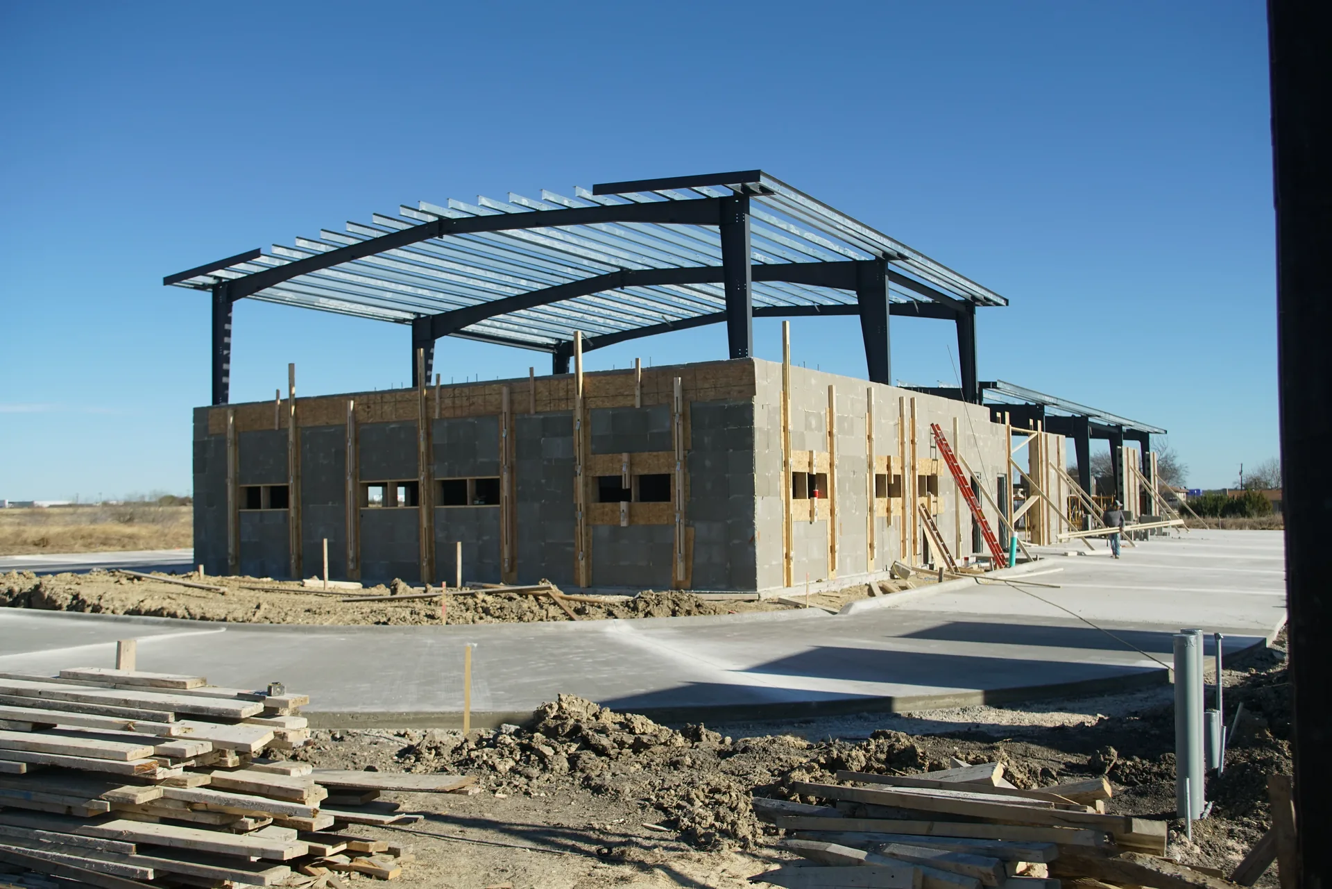 Red-iron steel building frame erected on a concrete slab with galvanized purlins in place under a clear Texas sky